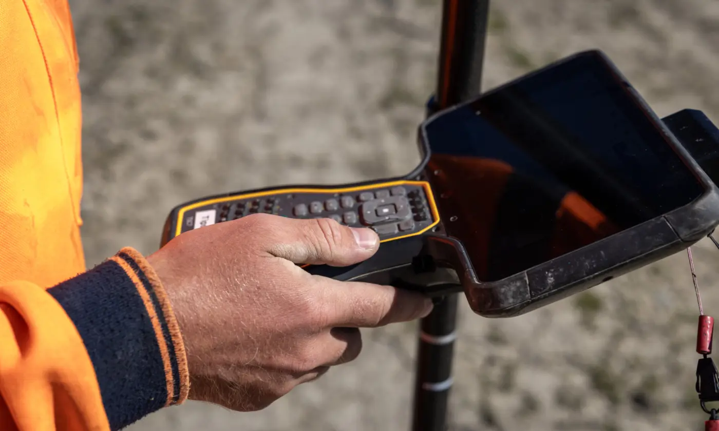 An Eliot Sinclair surveyor on site using a handheld data collector paired with GPS equipment to set out precise locations.